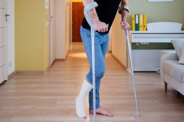 Koltuk değnekleriyle yürümeye çalışan yaralı bir adam. Kırık bir bacağın evde rehabilitasyonu.