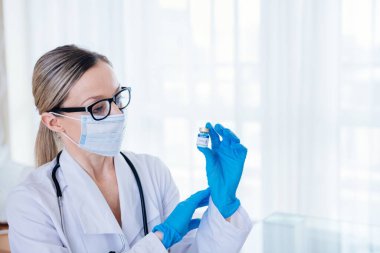 Female doctor in a protective mask and surgical gloves holding an ampoule with vaccine against covid-19.