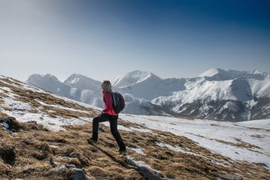 A woman hiker with a backpack is walking on a path in a mountain range in a beautiful winter landscape.