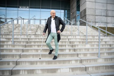 Yakışıklı yetişkin bir adam bastona yaslanır ve merdivenleri tırmanır..