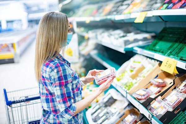 Female is choosing fresh vegetables and fruits in hypermarket during pandemic.