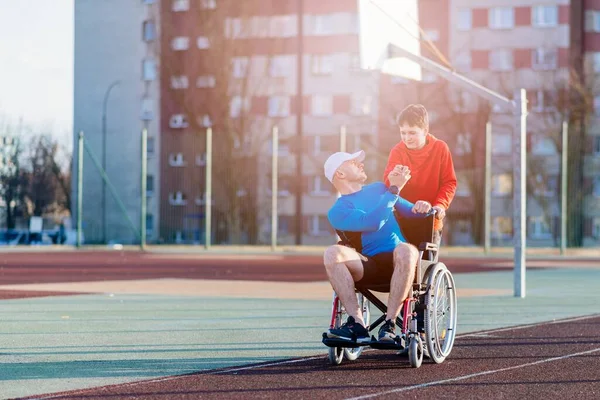 Behindertensportler im Rollstuhl schenkt Sohn High-Five auf Leichtathletik-Bahn. — Stockfoto