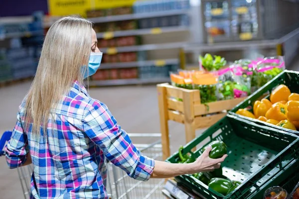 Compras durante una pandemia en el supermercado. Mujer con máscara protectora comprando vegetales en una tienda. —  Fotos de Stock