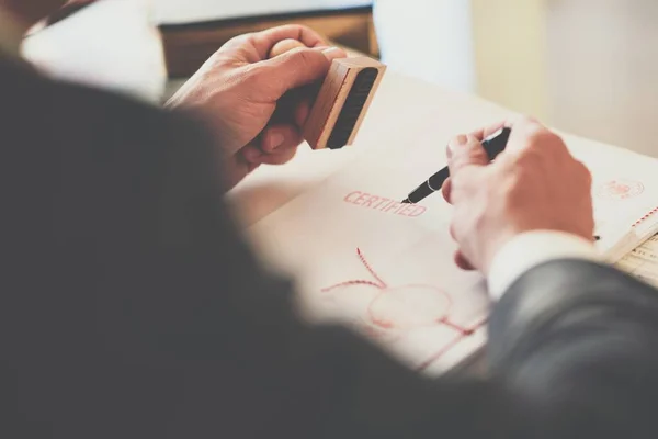 A close-up of the hand of a notary who stamps the document by hand and signs it with a pen. — Stock Photo, Image