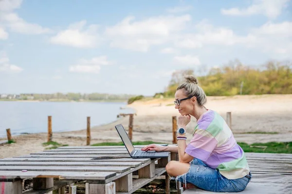 Selbstständiges Berufswahlkonzept im Internet: Eine junge Frau arbeitet am Laptop am See. — Stockfoto