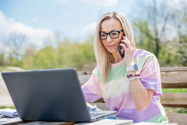 Blondes Mädchen arbeitet draußen mit Laptop und Handy bei schönem sonnigen Wetter. — Stockfoto
