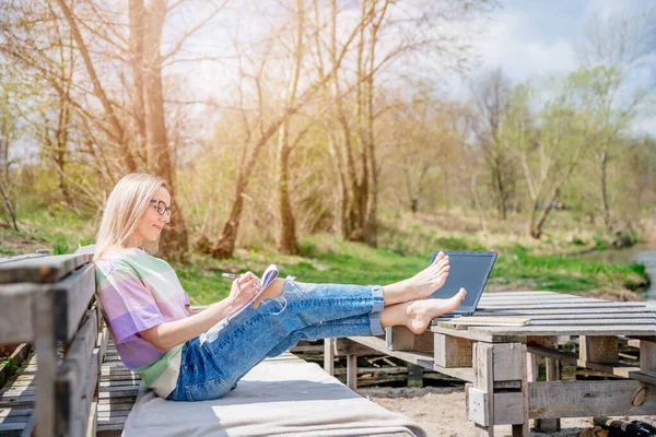 Blondes Mädchen mit Beinen auf einem Palettentisch arbeitet an einem schönen sonnigen Tag im Freien. — Stockfoto