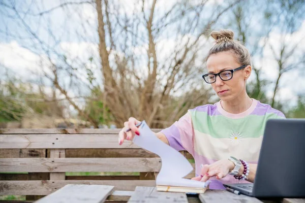 Frau mit Brille arbeitet draußen mit Laptop. Sie macht die Notizen. — Stockfoto