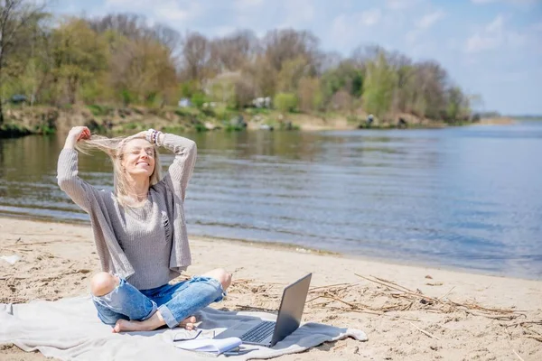Szczęśliwa wolna kobieta z laptopem na plaży nad jeziorem. — Zdjęcie stockowe