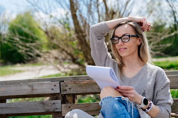 Pensiv kvinnlig konstnär med skissbok avkopplande utomhus tänker på kreativitet. — Stockfoto