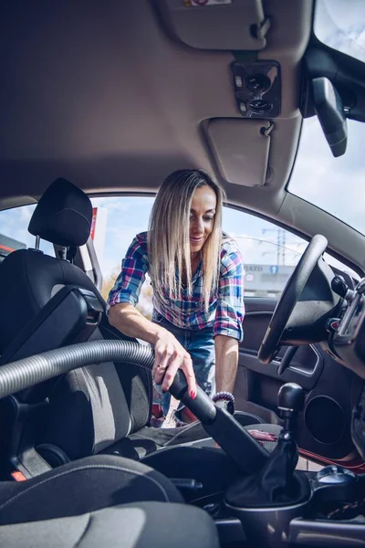 笑顔ブロンドの女性は、掃除機で車のインテリアをきれいにします,洗車. — ストック写真