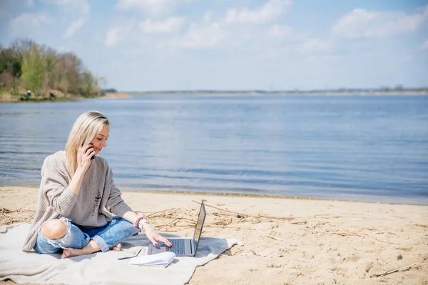 Blonde occupée travaille à distance par une belle journée ensoleillée au bord du lac. — Photo