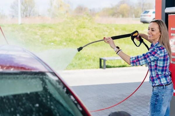 Beauty woman at the self-service car wash station washing the foam off her car. — 스톡 사진