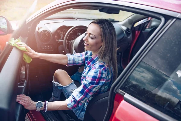 A woman in checkered shirt cleans the inside of the car with a microfiber cloth. — Stockfoto