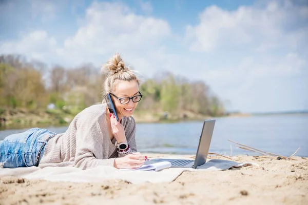 Beauty smiling woman using laptop computer on a beach. Girl freelancer working by a lake. ロイヤリティフリーのストック写真