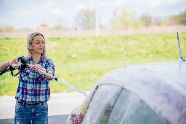 Žena na self-service myčka aut stanice mytí pěny z jejího auta. — Stock fotografie