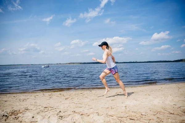 A sporty woman runing on the shore of a lake in sportswear. — Stock Photo, Image