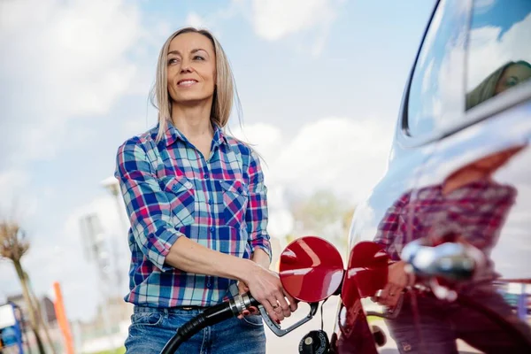 Lächelnde blonde Frau füllt ihr Auto an einer Tankstelle mit Benzin. — Stockfoto