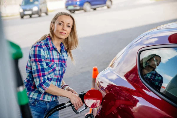 Mujer bonita está llenando su coche rojo con gasolina en una gasolinera. —  Fotos de Stock