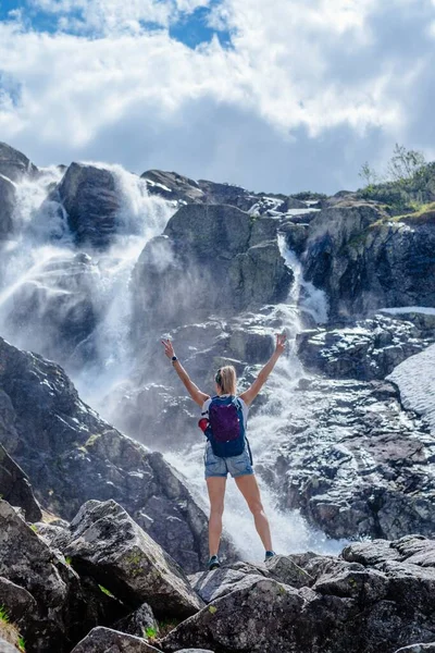 Vue arrière du touriste féminin avec les bras levés au-dessus de la belle cascade. — Photo