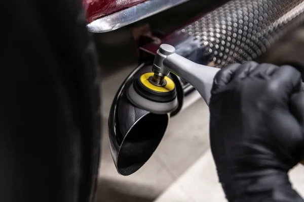 Car detailing studio worker polishes the chrome exhaust