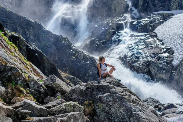 Bella turista è seduto su una roccia sopra la cascata Siklawa nelle montagne polacche Tatra. — Foto Stock