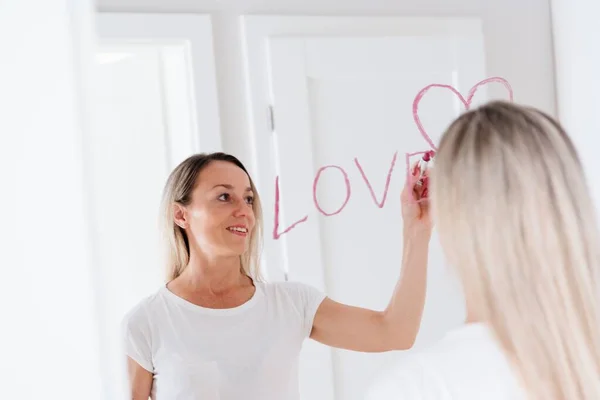 Donna positiva disegno a forma di cuore sullo specchio a casa. Concetto amore. — Foto Stock