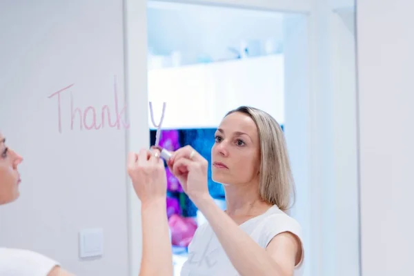 Una mujer escribe la palabra gracias en el espejo con un lápiz labial. — Foto de Stock