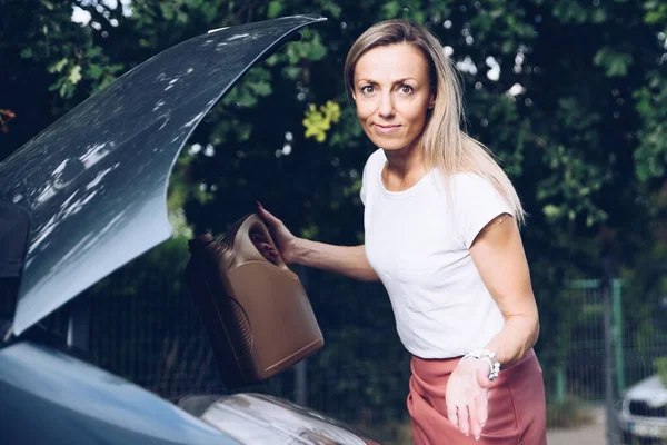 Eine blonde Frau weiß nicht, wo sie Motoröl in ihr Auto gießen soll. — Stockfoto