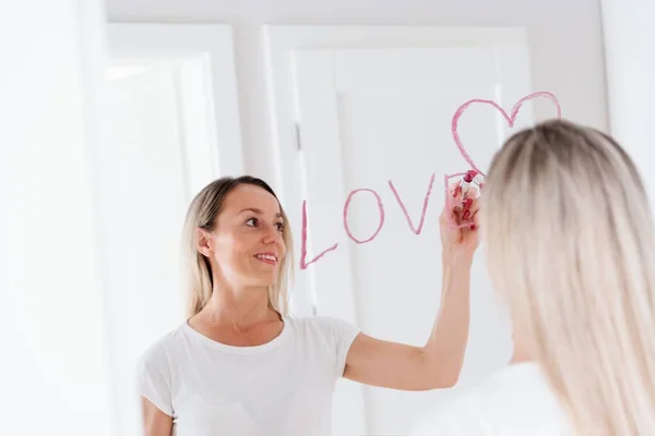 Mujer escribiendo en el espejo con lápiz labial. Inscripción pintada Te amo — Foto de Stock