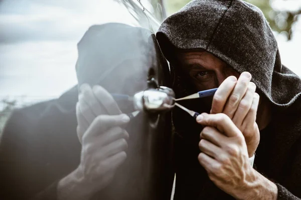 Een autodief die een autodeur opent met een slotenmaker. — Stockfoto