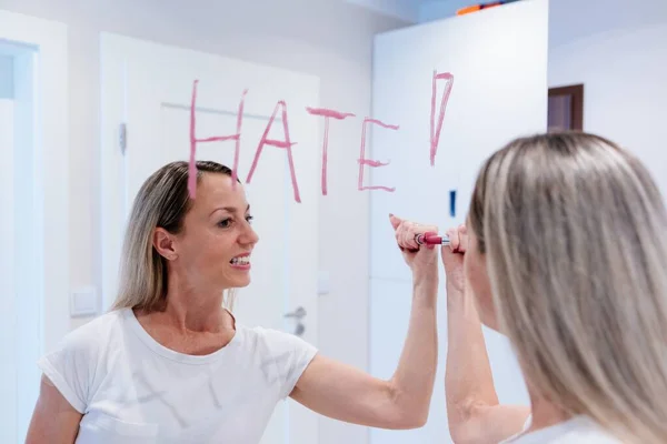 Donna che scrive odio su uno specchio con il rossetto. — Foto Stock