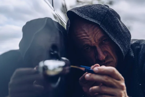 Maskovaný lupič se snaží dostat do auta. On odemyká auto paklíčem.. — Stock fotografie