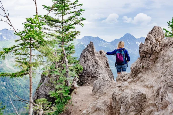 Visão traseira de uma mulher loira viajante entre rochas nas montanhas. — Fotografia de Stock