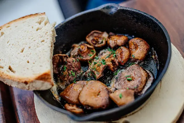 Sartén de champiñones y rebanada de pan sobre tabla de madera. —  Fotos de Stock