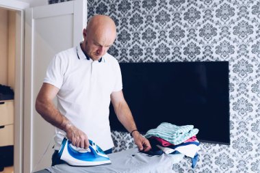 Ütü masasında ütü yapan adam mavi bir ütüyle.