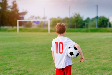 8 years old boy child holding football ball on playing field. 