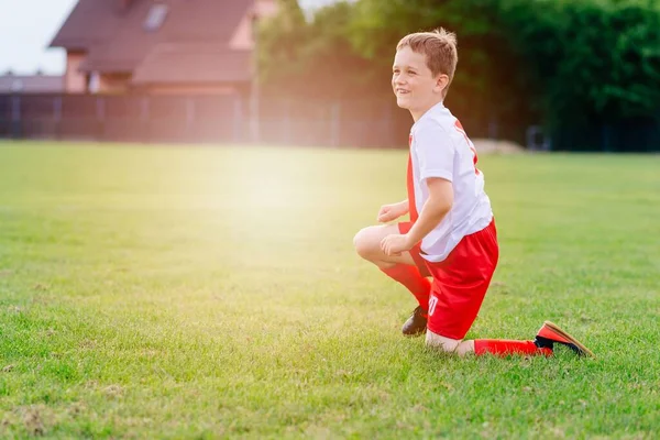 Little player in red shorts and a white t-shirt on the playing field. — Stok fotoğraf