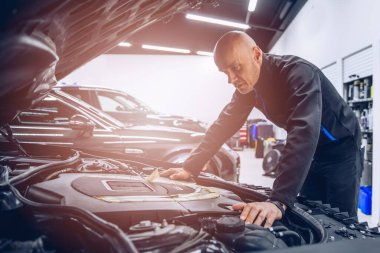 Mechanic in automobile service checking and inspecting car engine