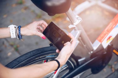 Girl in summer city using phone to unlock a city bike in the city.