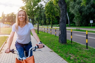 A pretty young woman in a white t-shirt is riding a city bike.