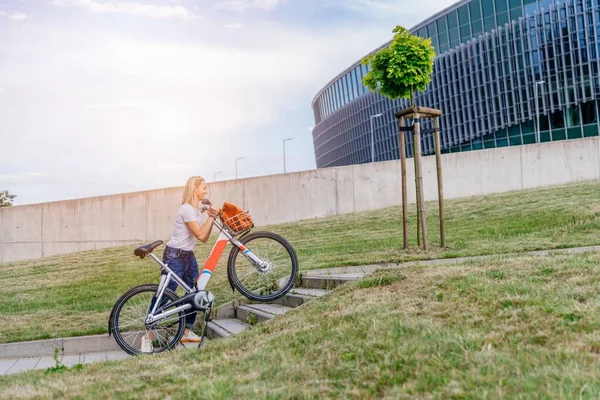 The woman is walking up the stairs with the city bike.