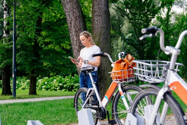 A young stylish woman uses a mobile application to rent a bike. — Zdjęcie stockowe