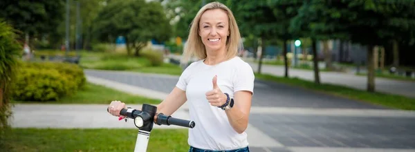 Woman with electric kick scooter standing on city street making a thumb up gesture. — Stock Photo, Image