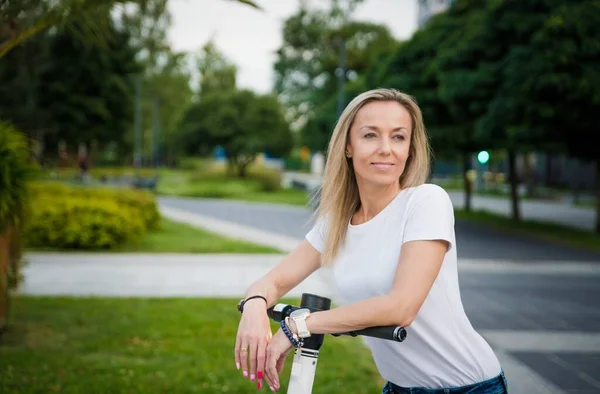 Een glimlachende vrouw op een scooter. Elektrisch vervoer, ecologisch vervoer. — Stockfoto
