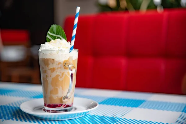 Iced latte coffee in a tall glass with white chocolate syrup, whipped cream and mint leaf. — Stock Photo, Image