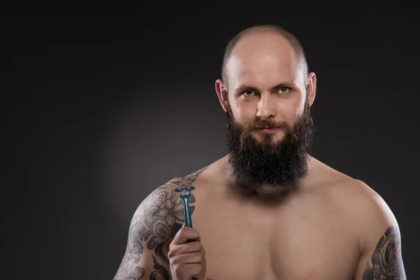 Homem careca muscular com uma barba segurando uma navalha — Fotografia de Stock