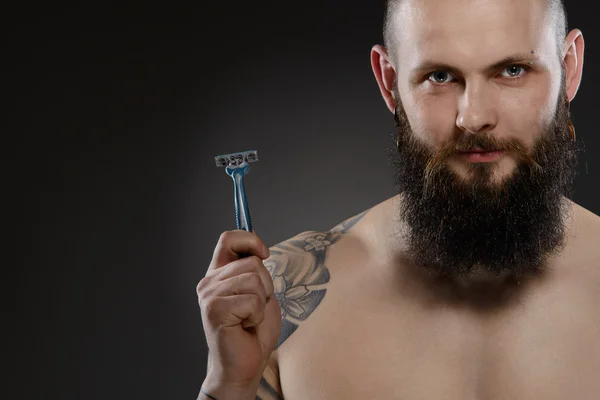 Muscular man with a beard holding a razor — Stock Photo, Image