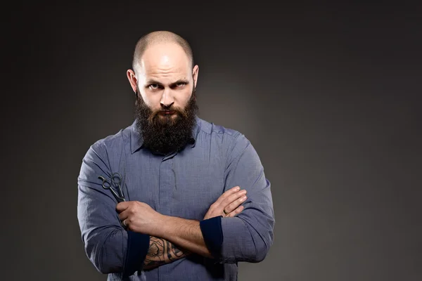 Un uomo calvo con la barba che tiene un paio di forbici. mani incrociate — Foto Stock