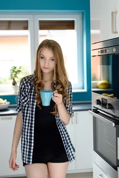 Glad blondin kvinna med en kopp kaffe i hennes kök — Stockfoto